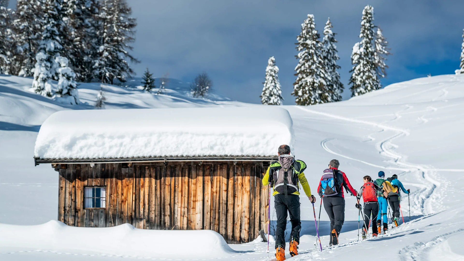 Group of ski tourers hiking in snow past a snow-covered wooden cabin