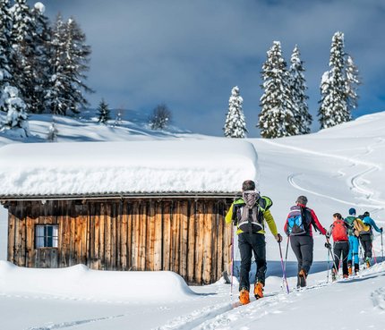 Sarntal – Skitouren im Herzen Südtirols © Carmen Moser Gruppe Skitourengeher wandert im Schnee an einer verschneiten Holzhütte vorbei