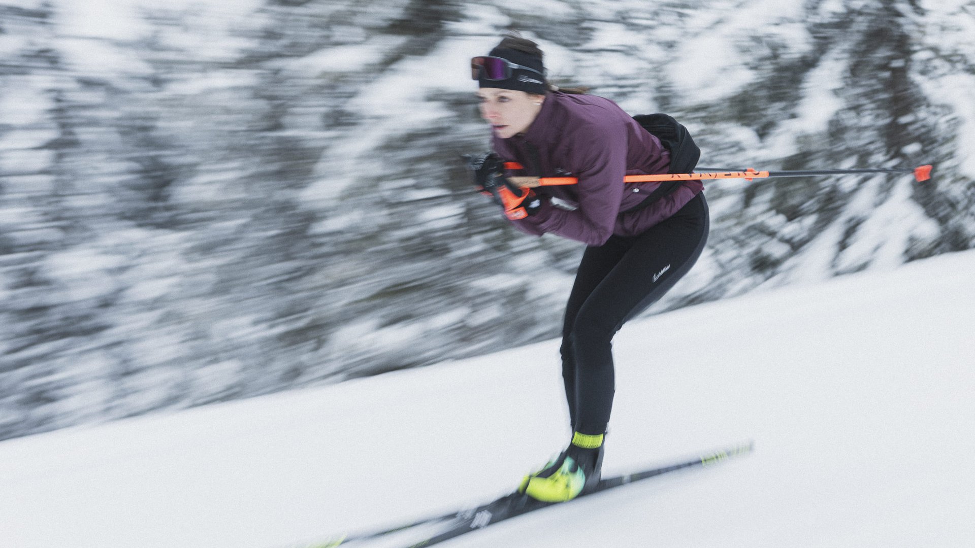 Frau beim Skilanglauf mit verschneitem Wald im Hintergrund