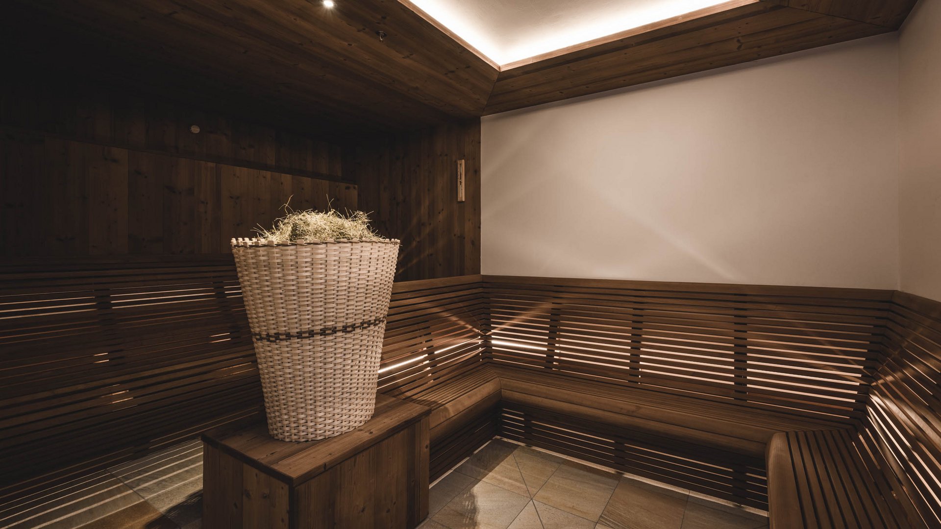 Innenraum einer Sauna mit Holzbänken und Korb mit Kräutern