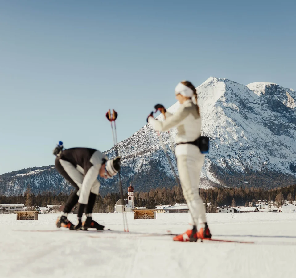 Zwei Langläufer auf verschneiter Loipe vor Alpenpanorama