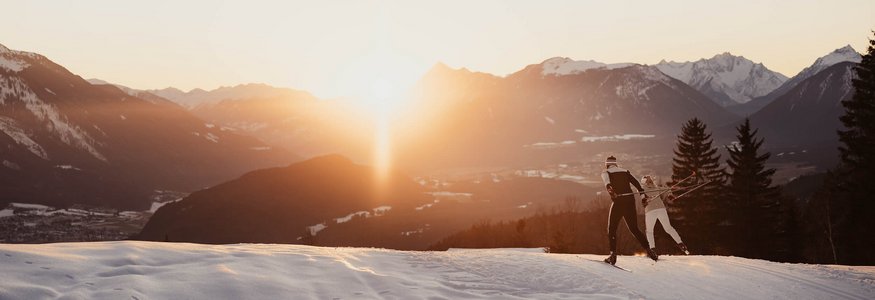 Two cross-country skiers on snowy mountain at sunset