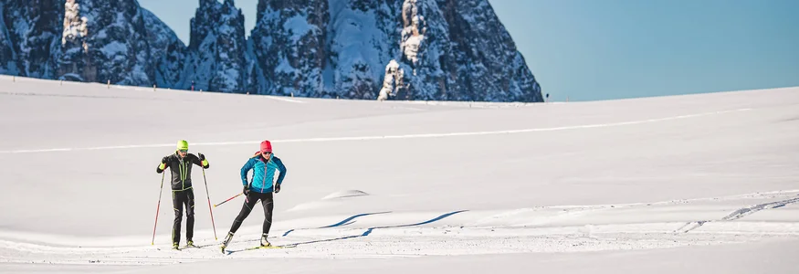 Langlauf & Kultur vereint auf der Seiser Alm © Seiser Alm Marketing - Werner Dejori Zwei Langläufer auf schneebedecktem Feld vor hohen, schneebedeckten Bergen