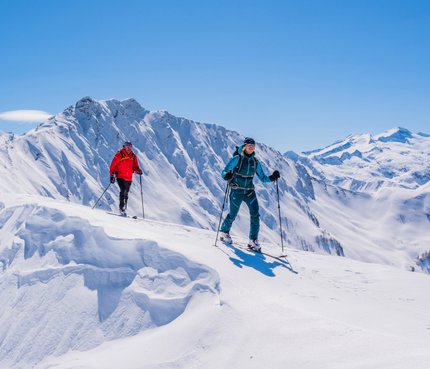 Zwei Skitourengeher in bunten Outfits wandern im sonnigen, verschneiten Gebirge