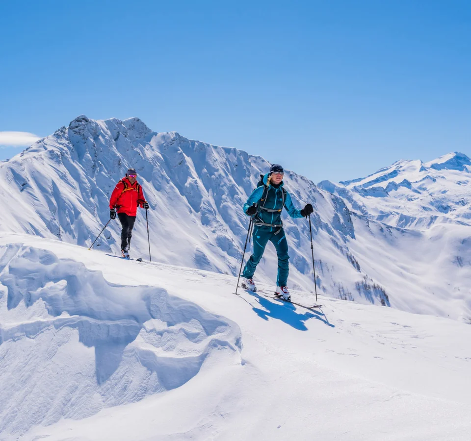 Zwei Skitourengeher in bunten Outfits wandern im sonnigen, verschneiten Gebirge