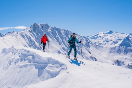 Zwei Skitourengeher in bunten Outfits wandern im sonnigen, verschneiten Gebirge