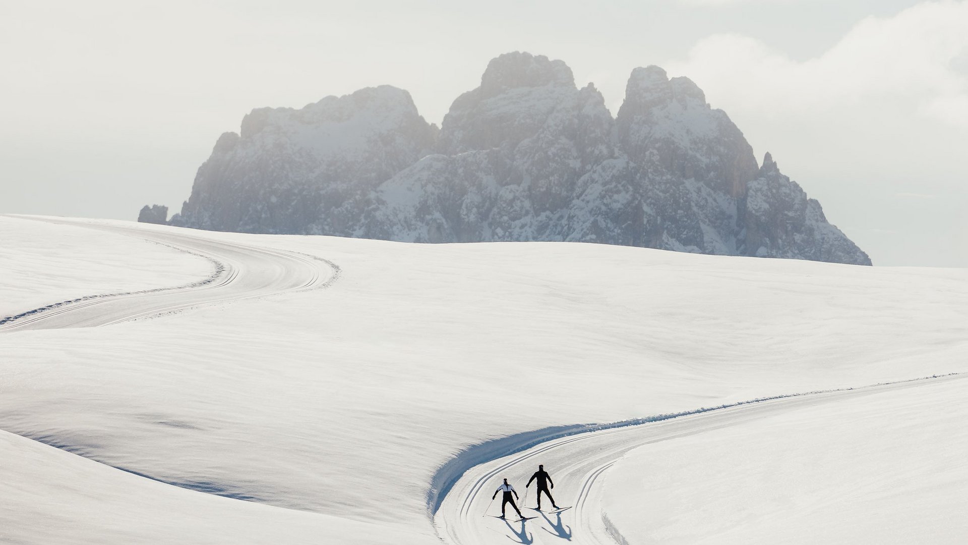 Zwei Langläufer auf einer verschneiten Spur mit Bergen im Hintergrund