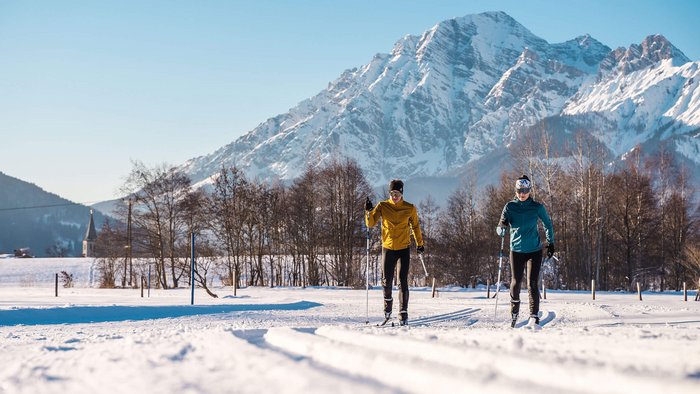 Zwei Langläufer auf Schnee mit Berg im Hintergrund bei sonnigem Wetter