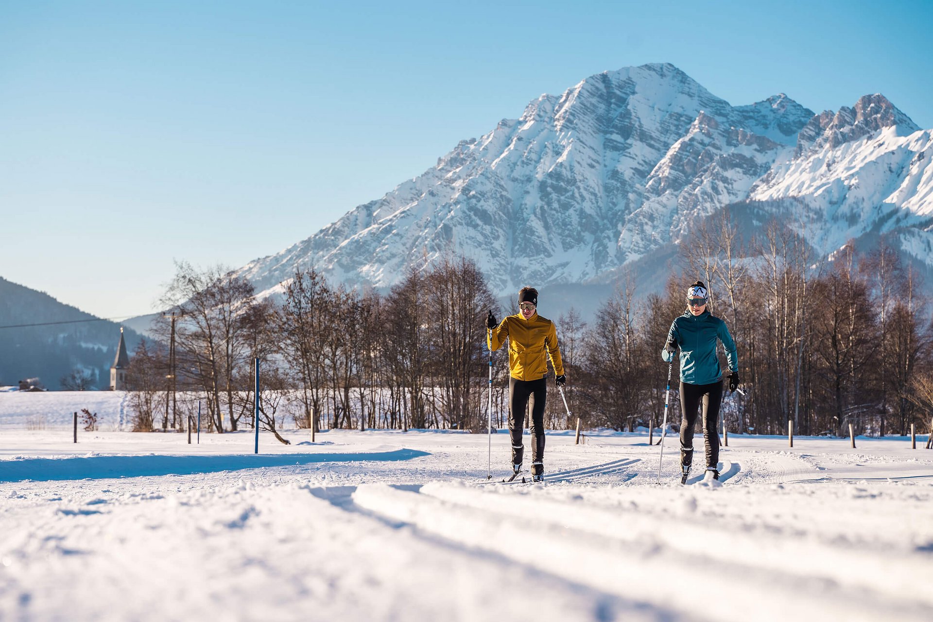 Zwei Langläufer auf Schnee mit Berg im Hintergrund bei sonnigem Wetter