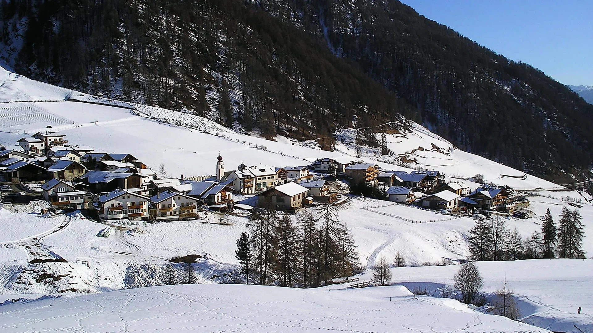 Verschneites Bergdorf mit Häusern vor einem bewaldeten Berghang
