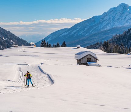 3 Highlights für den Langlaufurlaub in Nassfeld-Pressegger See | Lesachtal | Weissensee © Peter Maier Langläufer in verschneiter Alpenlandschaft mit Hütten und Bergen