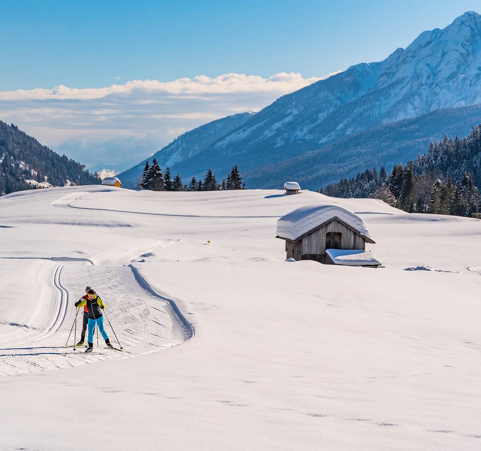 3 Highlights für den Langlaufurlaub in Nassfeld-Pressegger See | Lesachtal | Weissensee © Peter Maier Langläufer in verschneiter Alpenlandschaft mit Hütten und Bergen