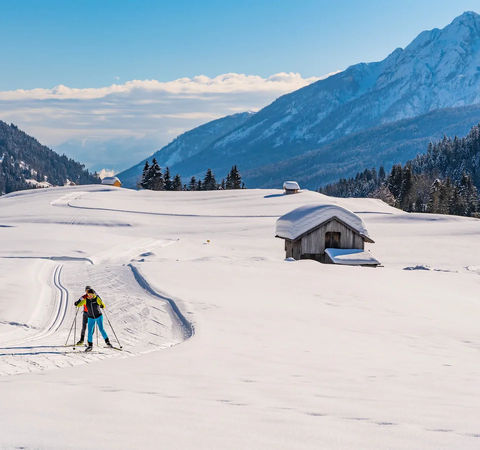 Langläufer in verschneiter Alpenlandschaft mit Hütten und Bergen