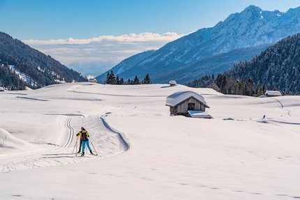 Langläufer in verschneiter Alpenlandschaft mit Hütten und Bergen
