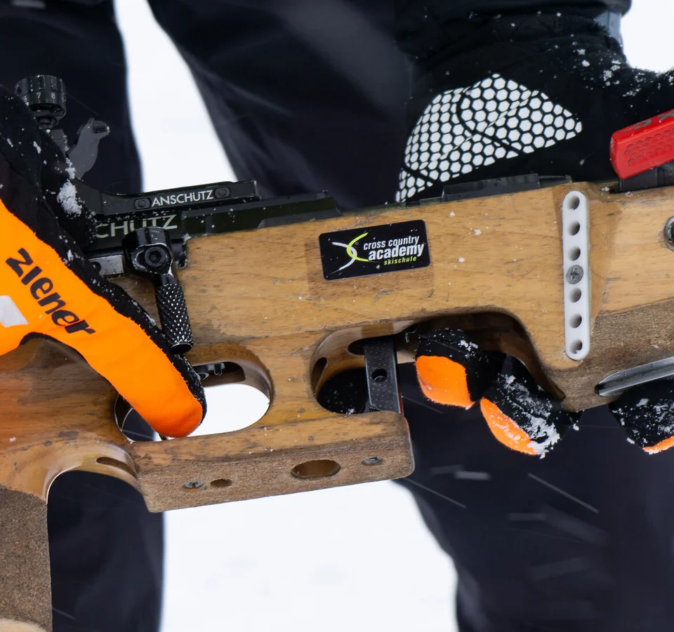 Person hält Biathlon-Gewehr mit orangenen Handschuhen im Schnee