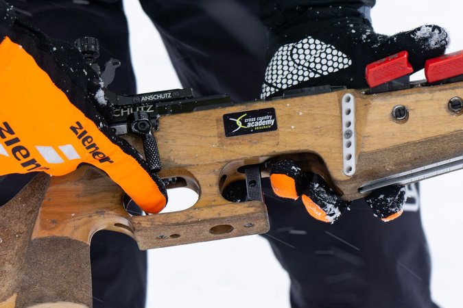 Person hält Biathlon-Gewehr mit orangenen Handschuhen im Schnee