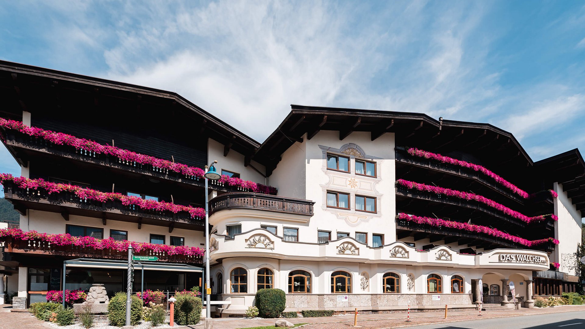 Hotel with balconies adorned with pink flowers under a blue sky
