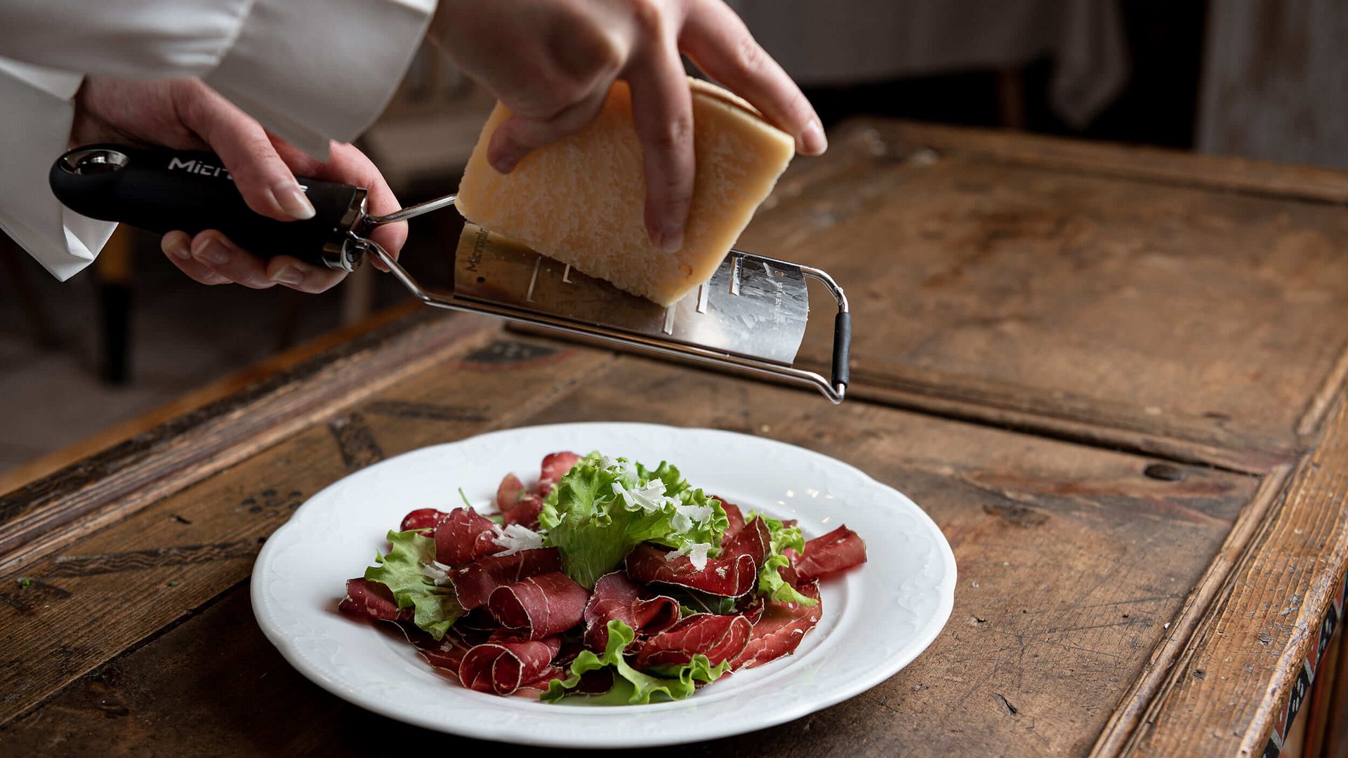 Parmesan wird über Rindfleisch mit Salat auf einem weißen Teller gerieben