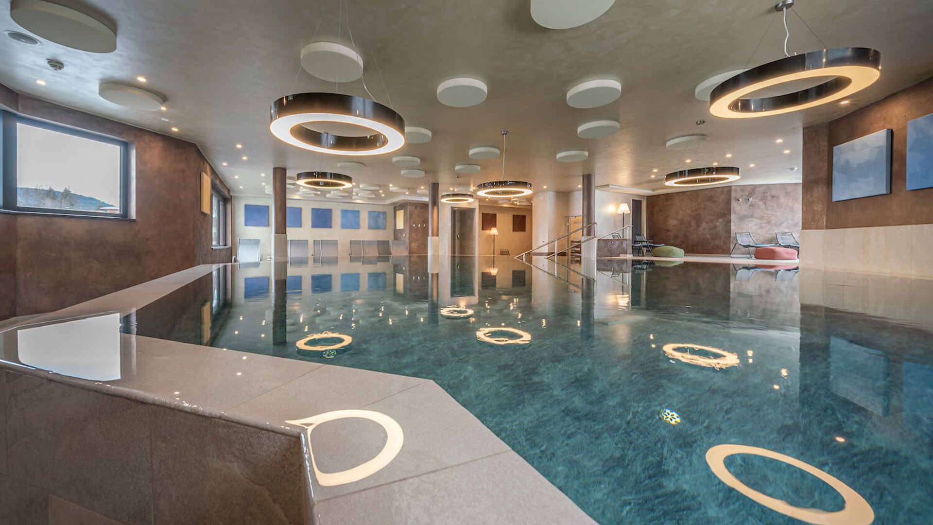 Modern indoor pool with circular ceiling lights and seating area