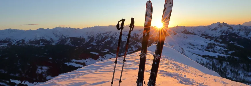 Skier und Skistöcke stehend im Schnee bei Sonnenuntergang in den Bergen