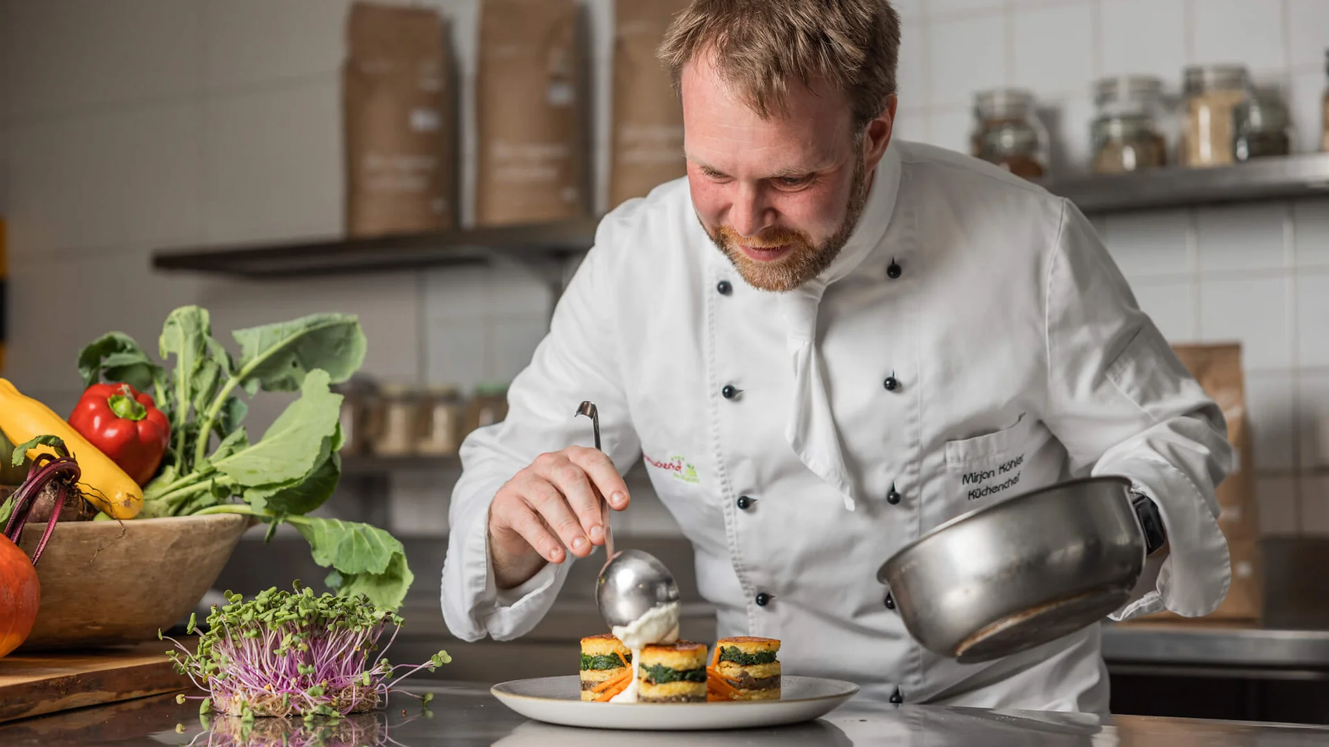 Koch in weißer Jacke richtet Teller mit kreativem Essen im Restaurant zu