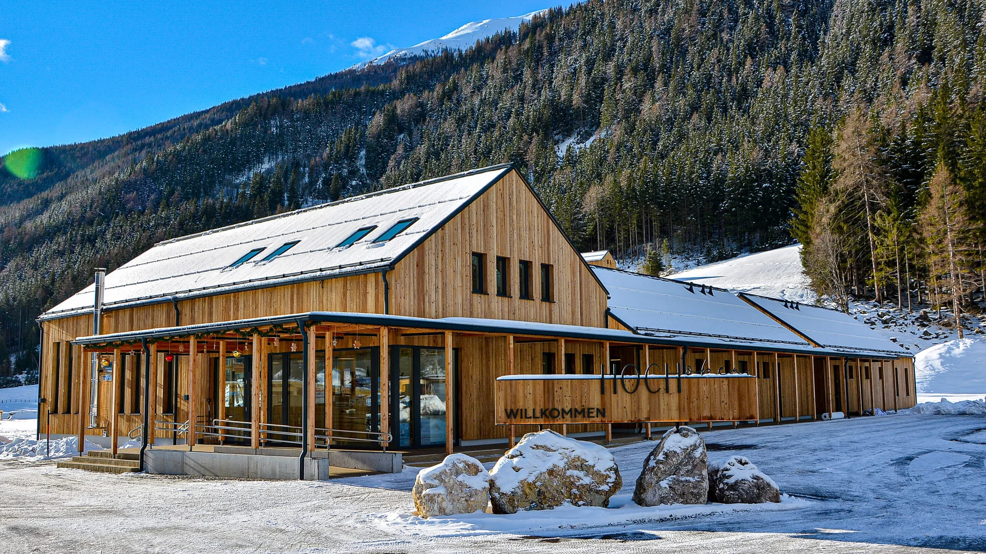 Holzgebäude im Schnee vor Waldbereich und Berg im Hintergrund