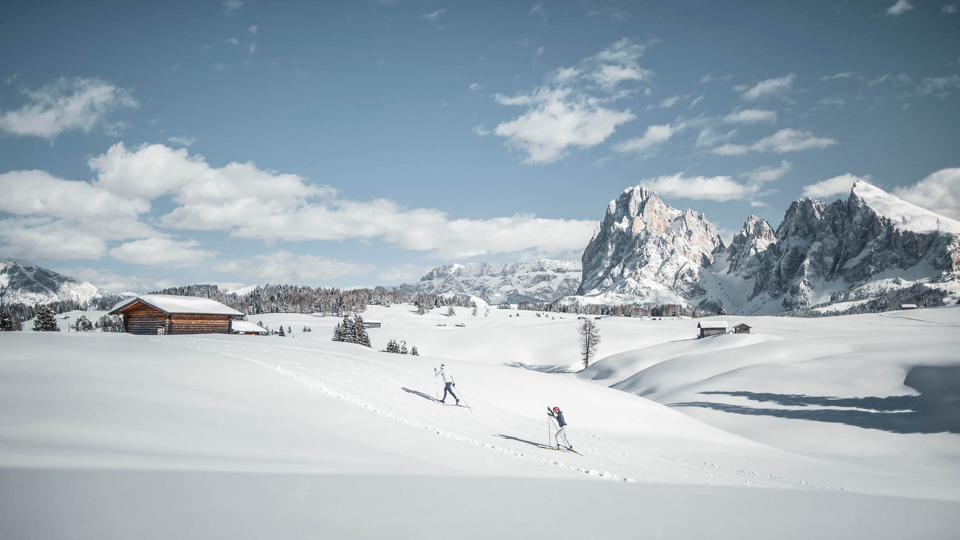 Zwei Skifahrer in verschneiter Berglandschaft mit Hütten und Gipfeln