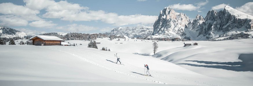 Zwei Skifahrer in verschneiter Berglandschaft mit Hütten und Gipfeln