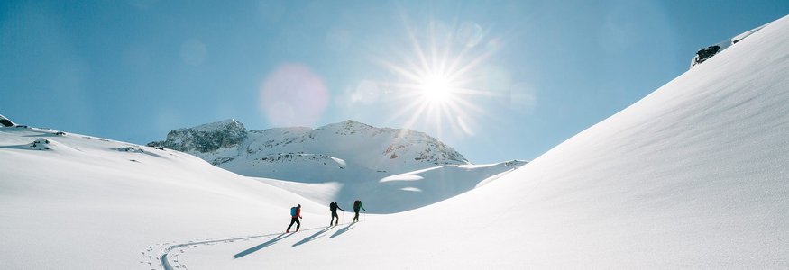 Drei Personen wandern im Schnee bei strahlendem Sonnenschein in den Bergen