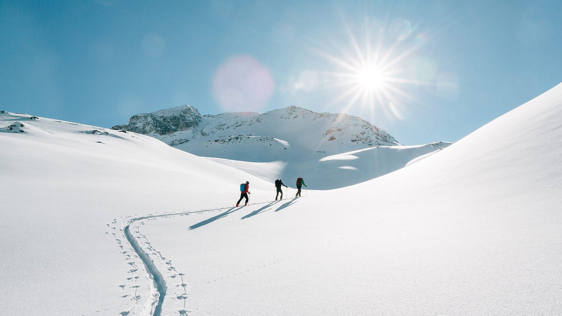 Three people hiking in snowy mountains under bright sunshine