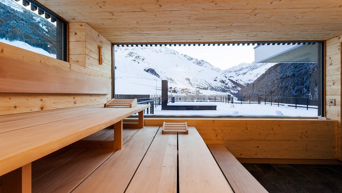 Innenraum einer Holzsauna mit Blick auf verschneite Berge und eine Terrasse