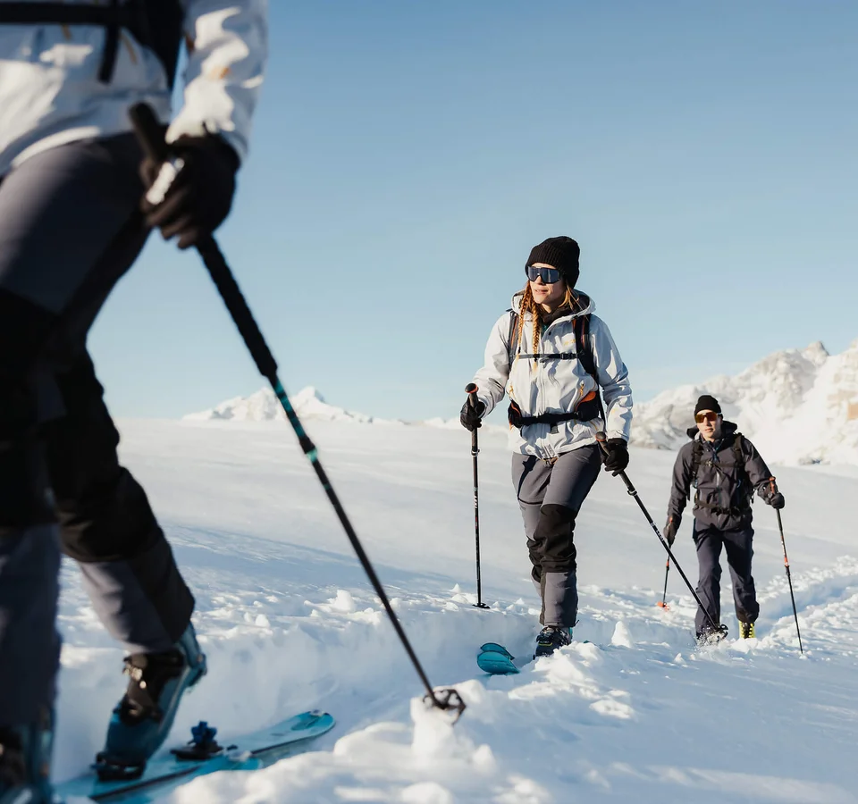 Drei Menschen beim Skitourengehen im verschneiten Berggebiet bei klarem Himmel