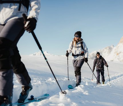 Drei Menschen beim Skitourengehen im verschneiten Berggebiet bei klarem Himmel