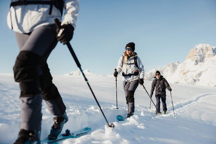 Drei Menschen beim Skitourengehen im verschneiten Berggebiet bei klarem Himmel