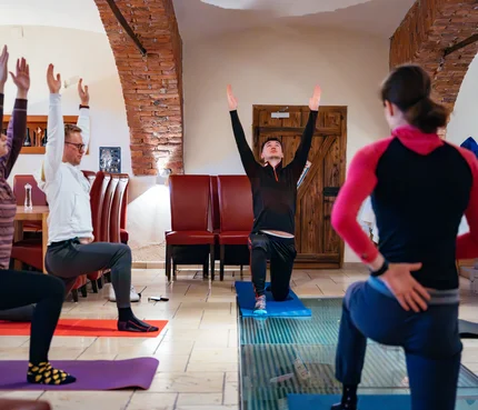 Gruppe übt Yoga in einem Raum mit Backsteinbögen und Matten auf dem Boden