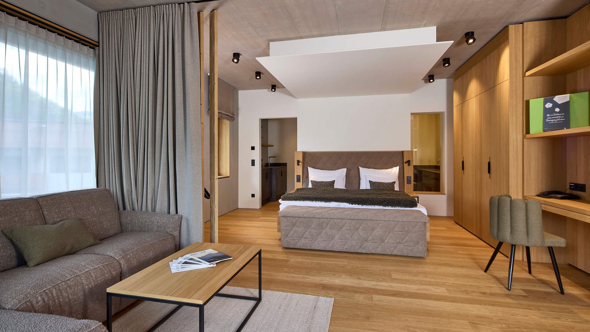 Modern hotel room with bed, sofa, desk, and wooden furniture