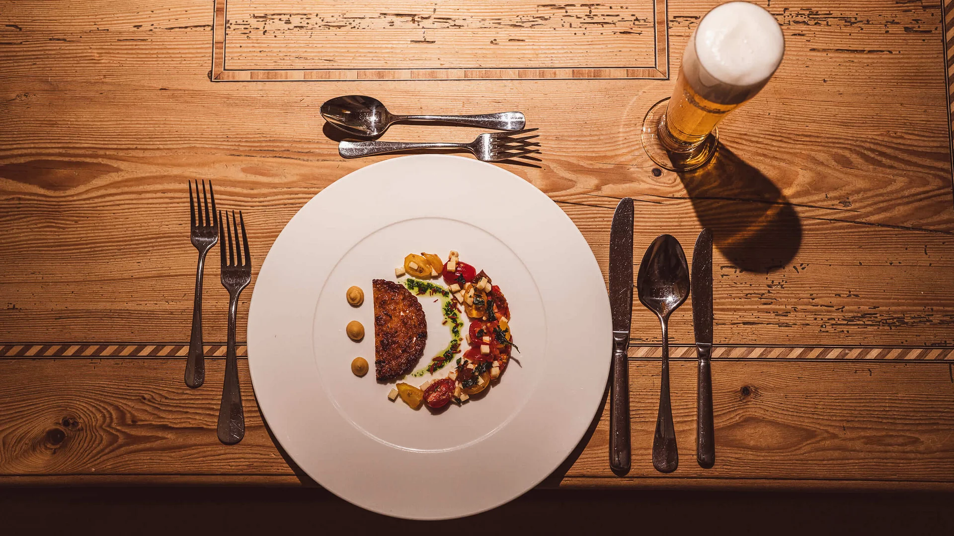 Hotel Kogler **** © Armin Ribis Fein angerichtetes Gericht mit Fleisch und Gemüse, Bier und Besteck auf einem Holztisch