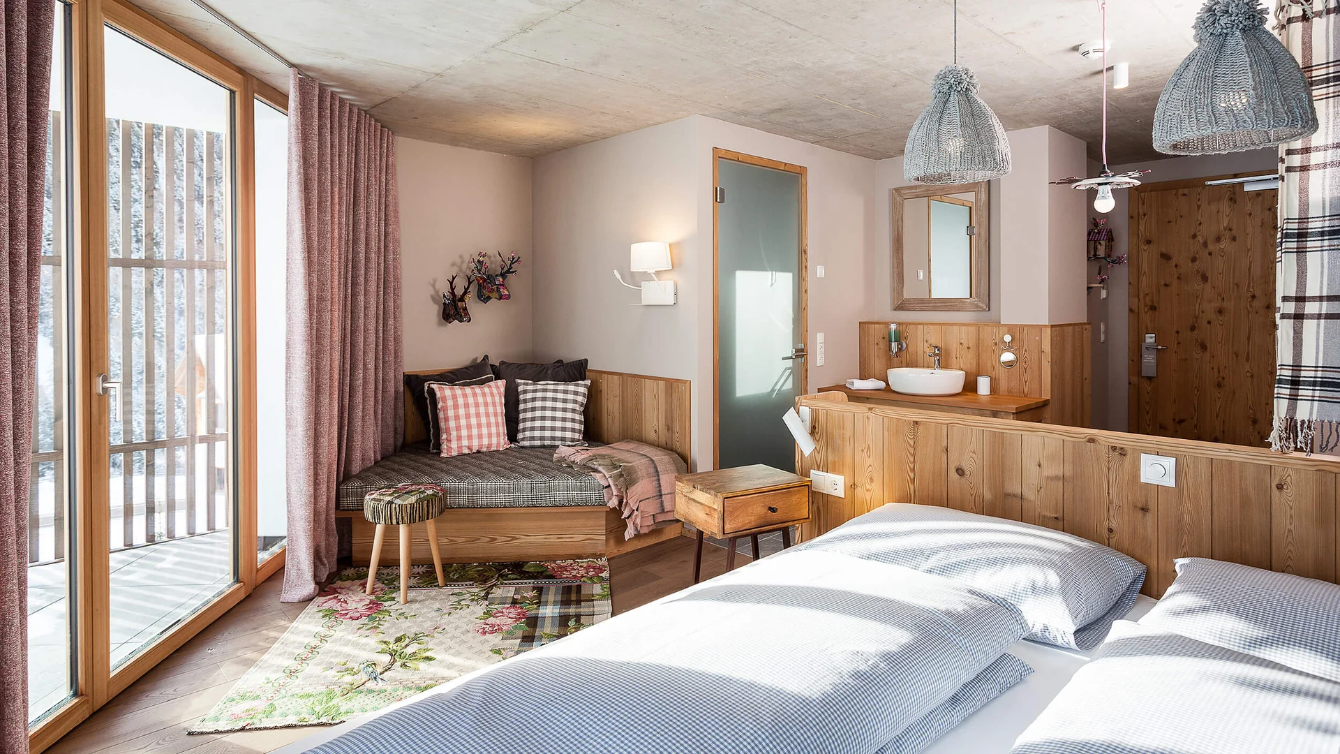Modern hotel room with wood decor, double bed and seating area next to balcony