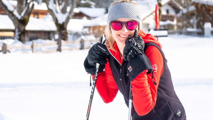 Lächelnde Frau mit Winterkleidung und Skistöcken im Schnee