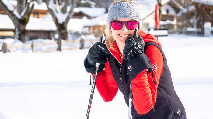 Lächelnde Frau mit Winterkleidung und Skistöcken im Schnee