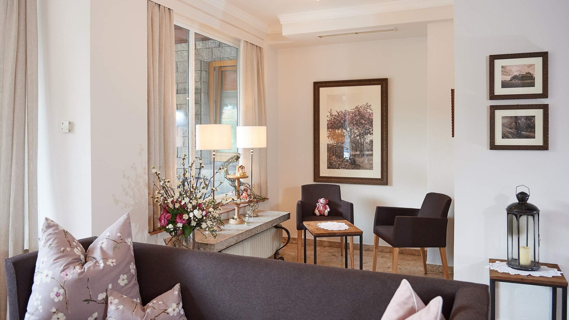 Cozy living area with sofa, chairs, flowers, and framed pictures on the wall