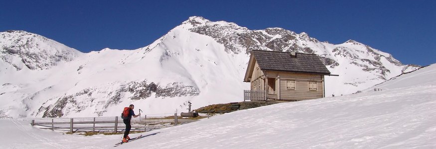 Skifahrer neben einer Holzhütte im verschneiten Berggebiet unter klarem blauem Himmel