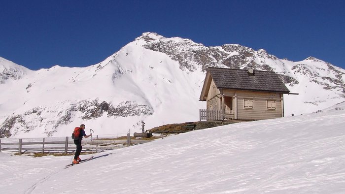 Skifahrer neben einer Holzhütte im verschneiten Berggebiet unter klarem blauem Himmel