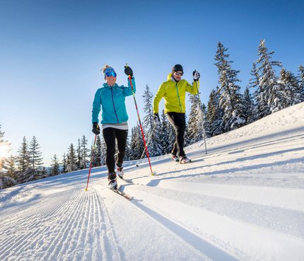 Zwei Personen beim Langlaufen auf verschneiter Loipe im Sonnenschein