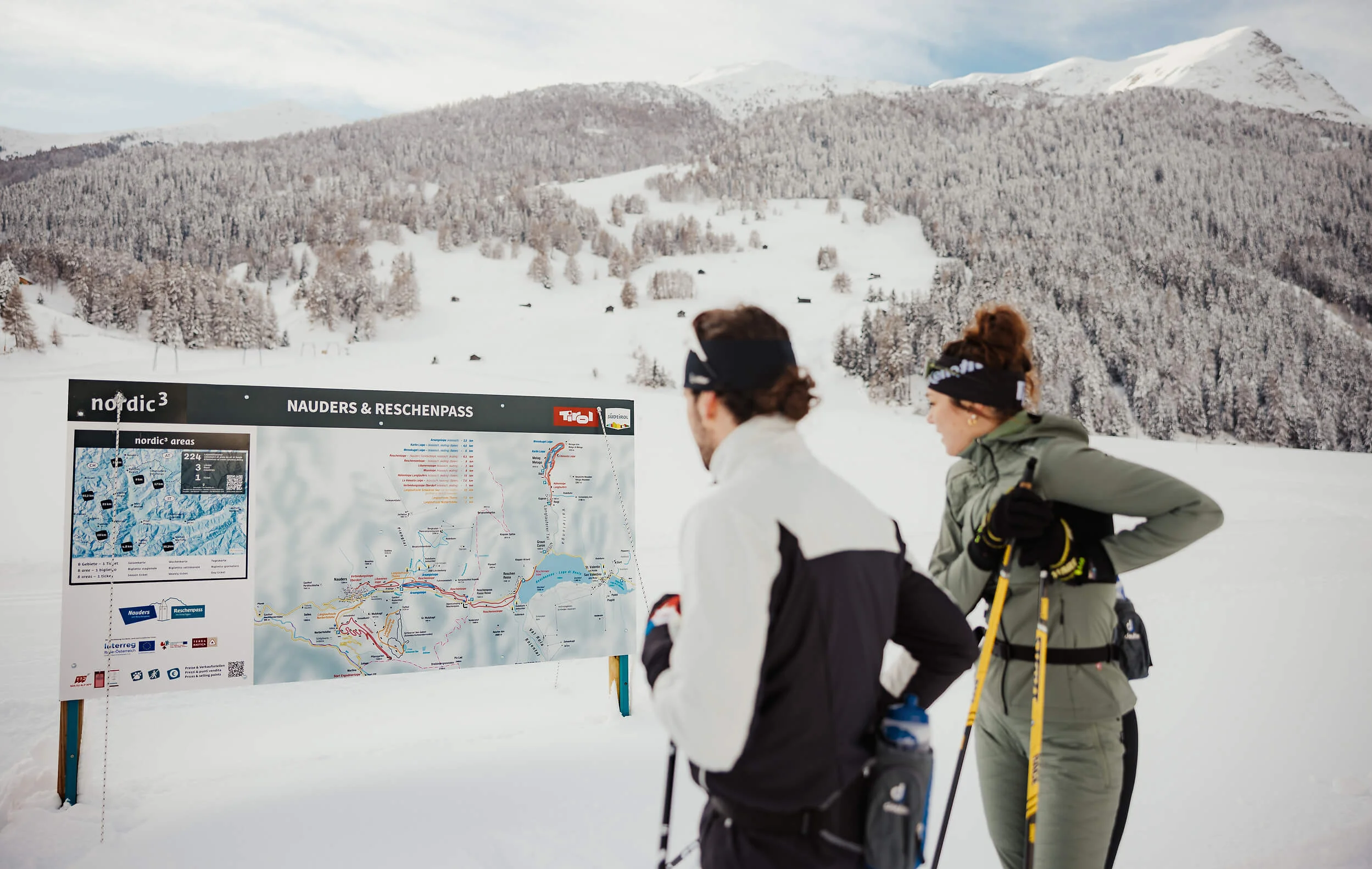 Italien © Alex Moling Zwei Skilangläufer schauen auf eine Karte von Nauders und Reschenpass im Schnee