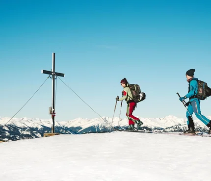 Murtal © Michael Koenigshofer Zwei Skifahrer mit Rucksäcken auf verschneitem Berggipfel neben Gipfelkreuz