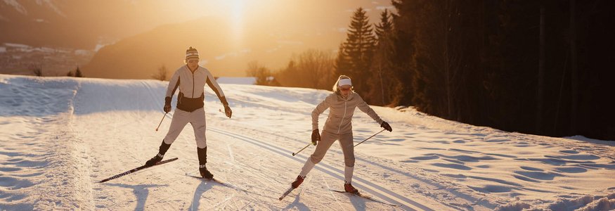 Two cross-country skiers skiing at sunset on snowy trail