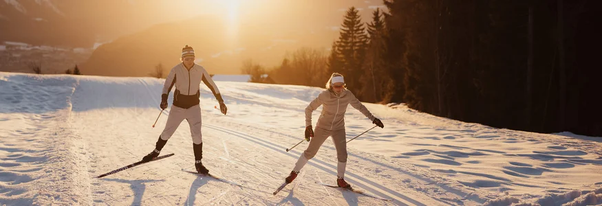 Two cross-country skiers skiing at sunset on snowy trail