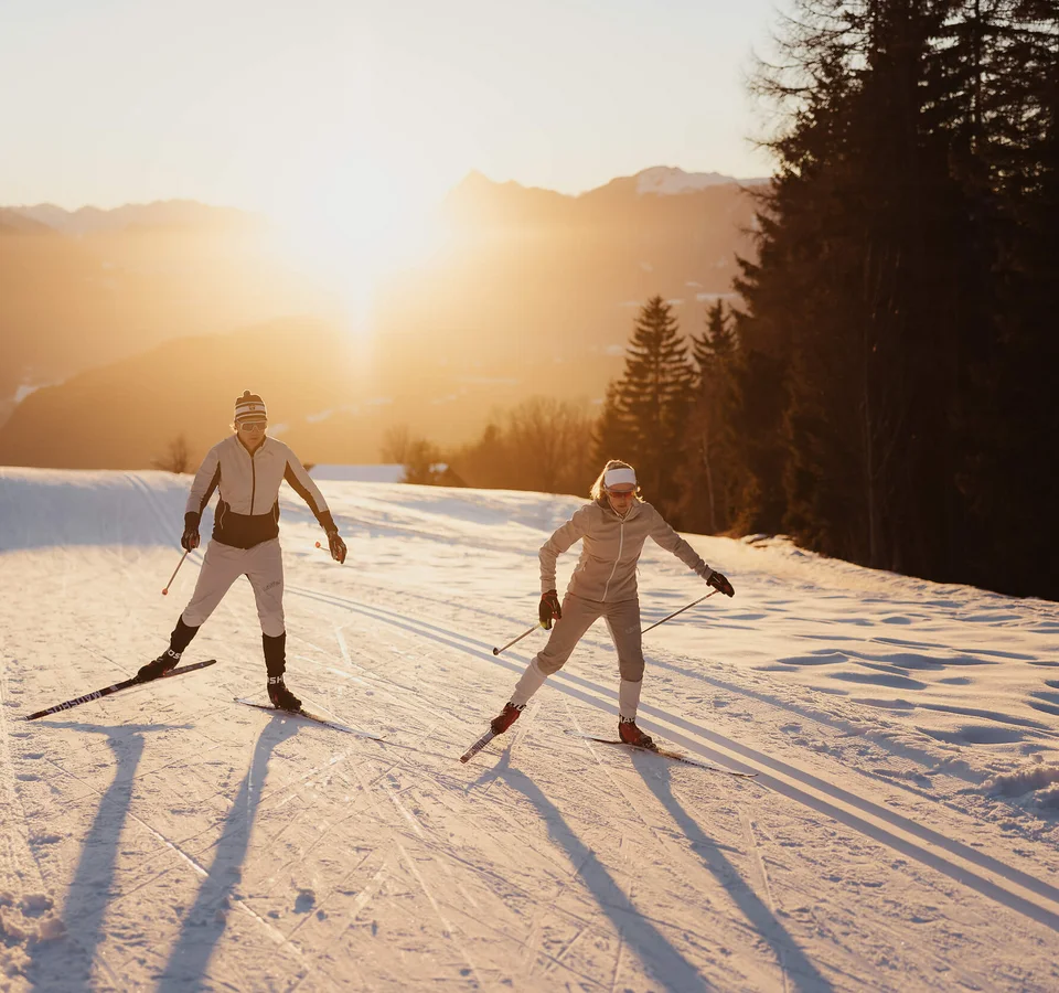 Two cross-country skiers skiing at sunset on snowy trail