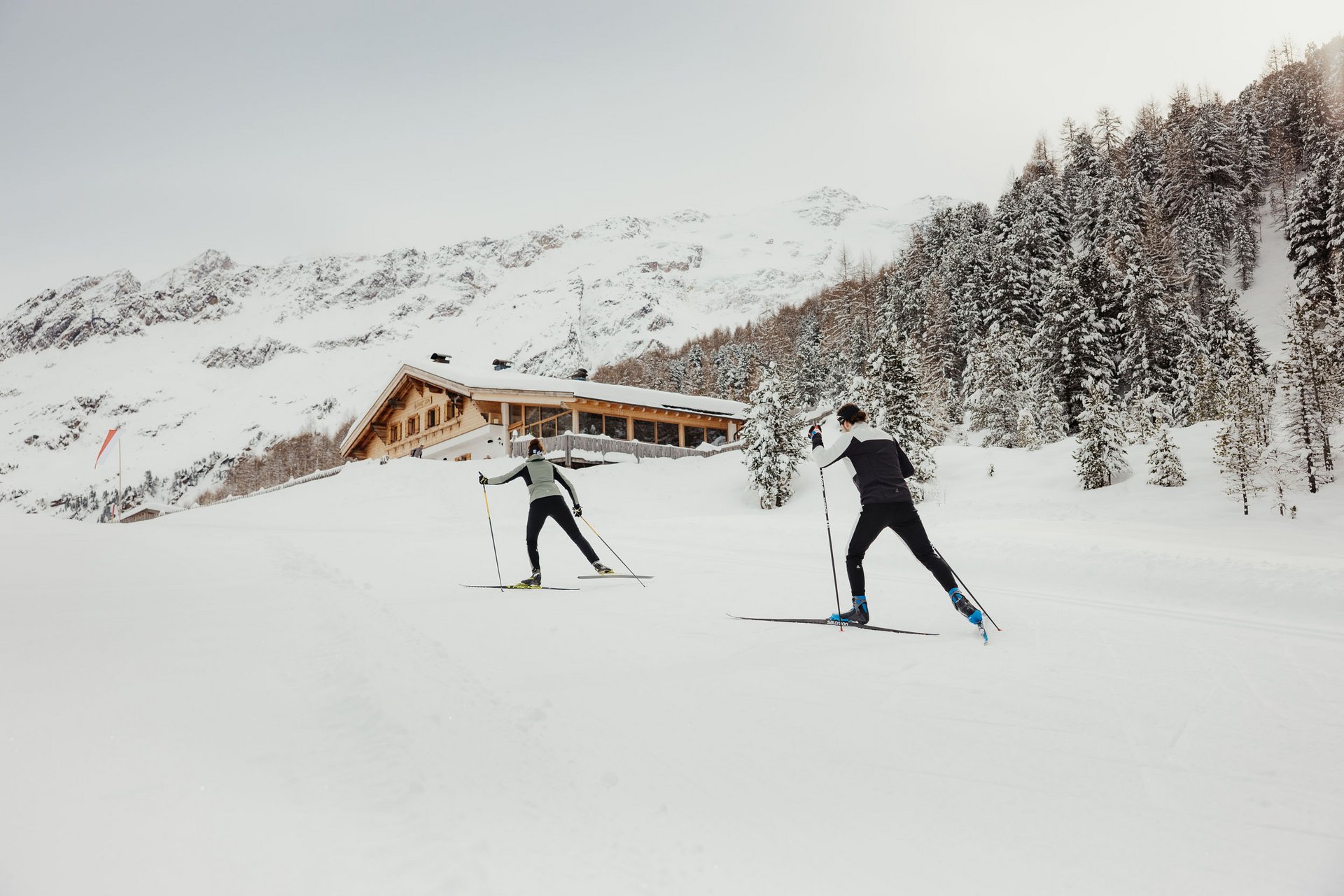 Zwei Langläufer vor verschneiter Berghütte im Winter